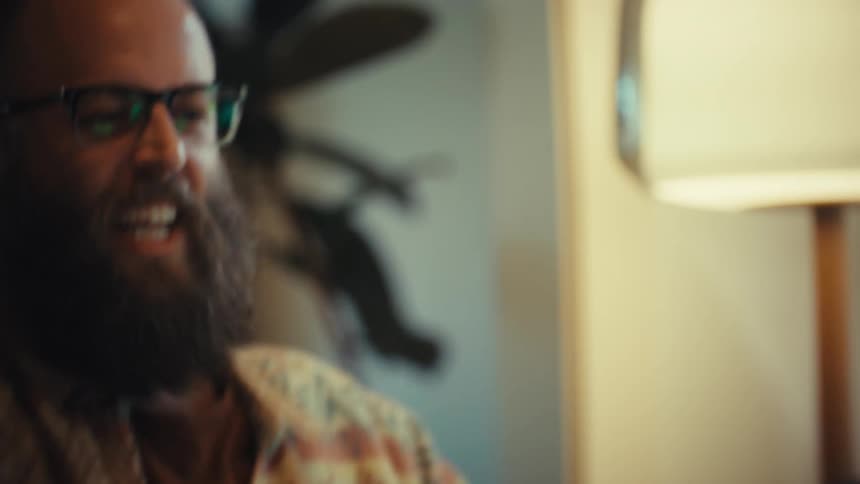 Close-up of a man with glasses and a beard whose video chat goes from happy to enraged