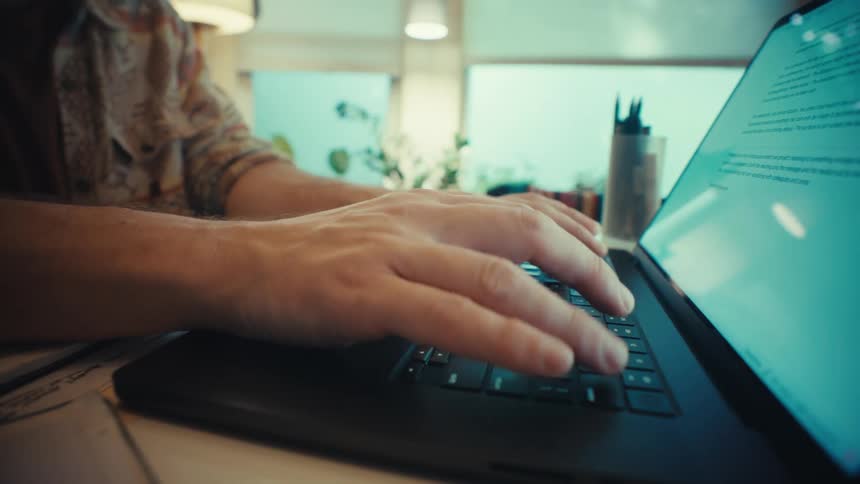 A slow dolly-out shot captures a man's hands typing on a laptop keyboard at his desk in an office