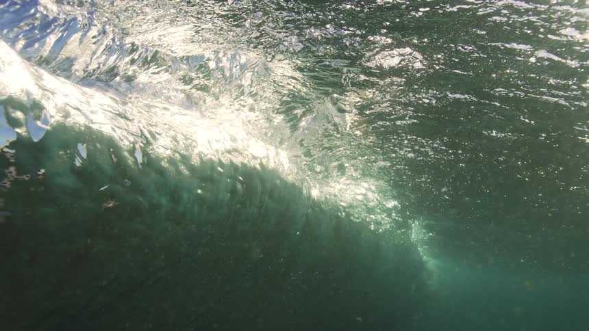A mesmerizing slow-motion underwater view captures the inside of a forming ocean wave illuminated by bright sunlight