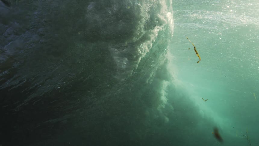 A stunning slow-motion underwater view captures a powerful ocean wave as it curls and crashes, creating a turbulent explosion of whitewater and bubbles