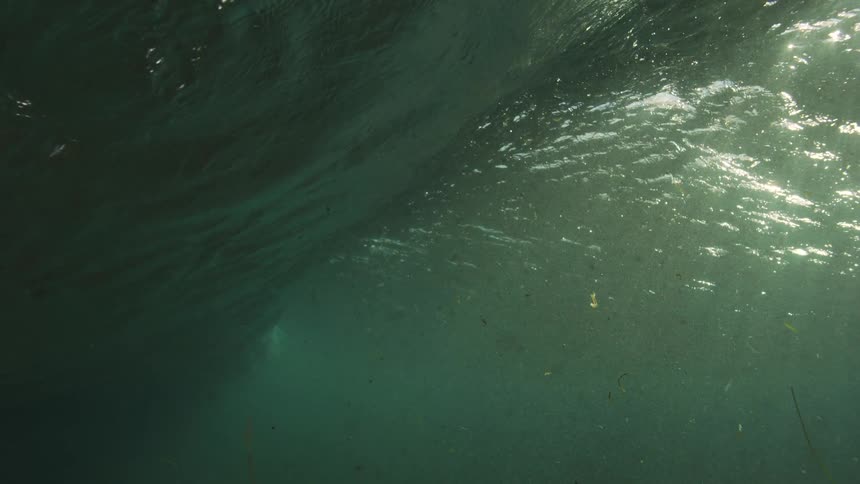 An ethereal underwater view captures the slow-motion formation of a wave, with sunlight filtering through the turbulent, particle-filled water