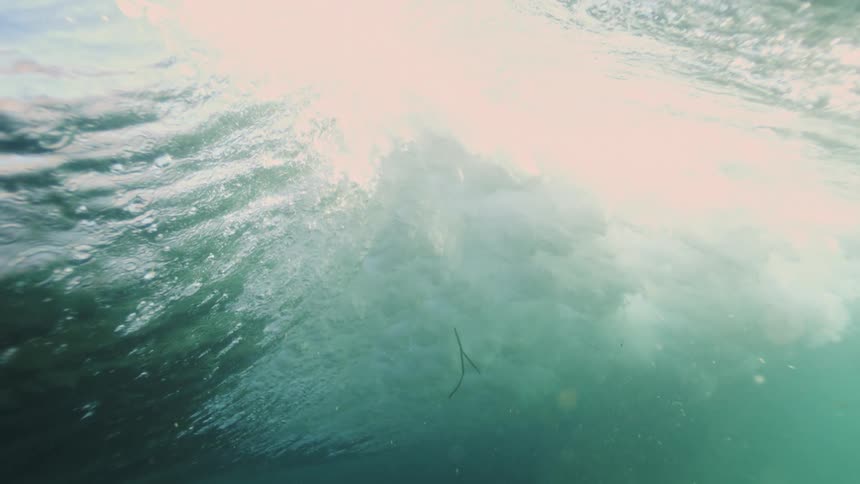 A slow-motion underwater view shows the majestic underside of a melting iceberg as sunlight streams through the turquoise arctic sea
