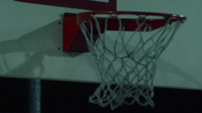 Close-up slow motion shot of an athletic man performing a powerful slam dunk on an outdoor basketball court at night