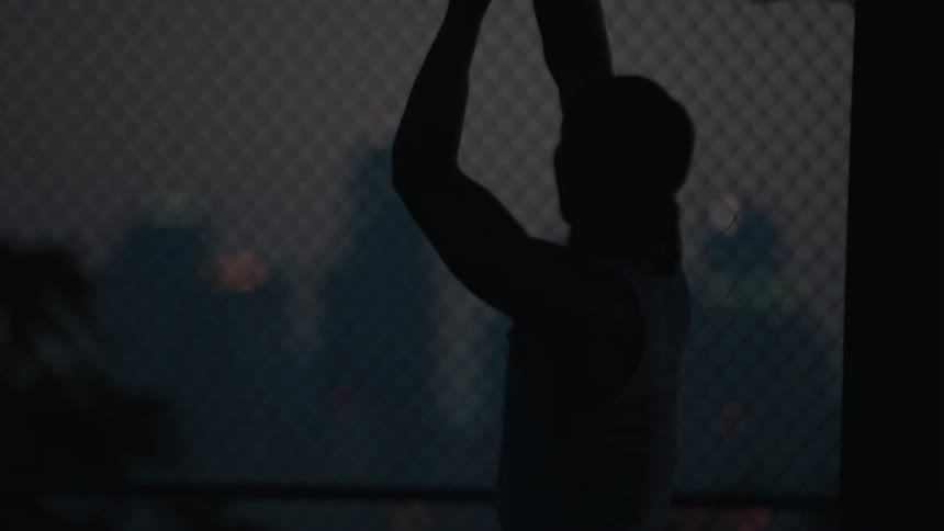 Silhouette of a basketball player practicing their free throw shot in slow motion on a city court at night
