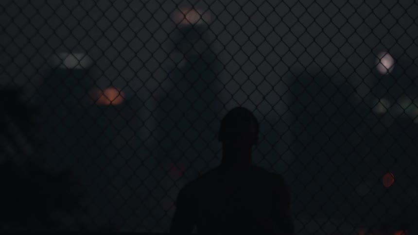 Slow motion silhouette of a man doing basketball tricks on a city court at night