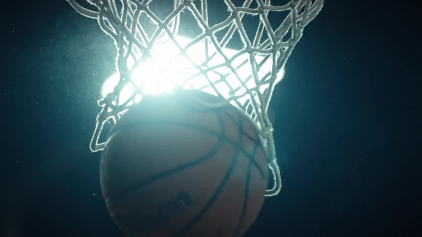 Dramatic slow-motion shot of a basketball falling through the hoop at night, illuminated by a bright light