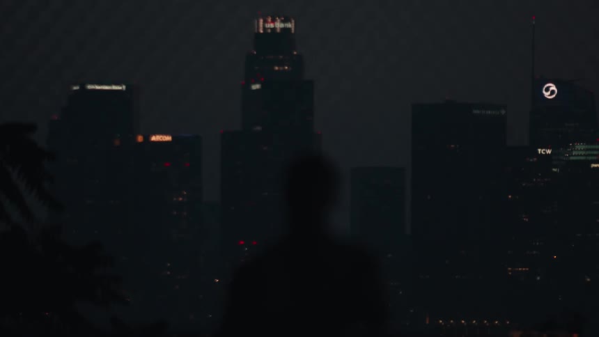 Two silhouetted friends play with a basketball in slow motion while overlooking the glowing skyline of Downtown Los Angeles at night