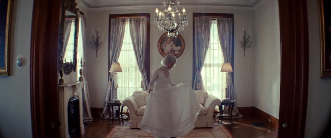 An elegant woman with white hair in a vintage wedding dress twirls gracefully in slow motion inside a classic living room