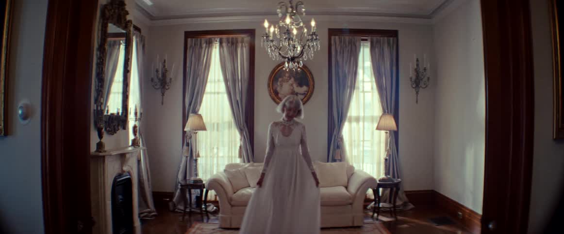A bride in a white gown stands in slow motion inside a lavish, sunlit room with vintage decor