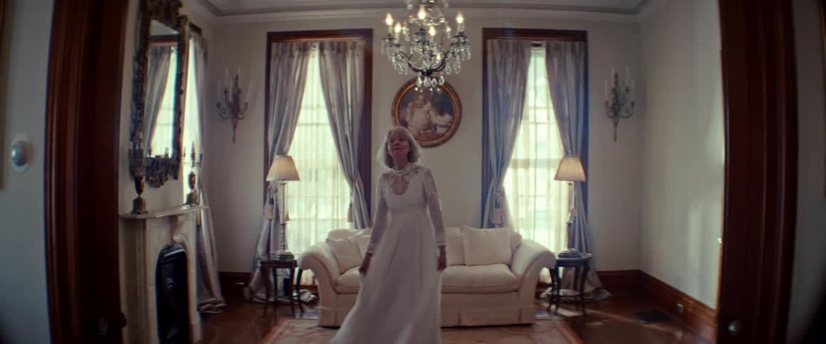 A graceful elderly woman in a beautiful white wedding gown twirls happily in a vintage-style living room
