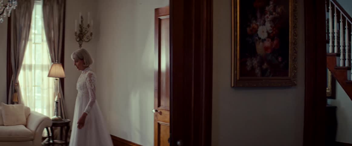 A melancholic elderly woman in a vintage wedding dress wanders through the elegant rooms of her classic home