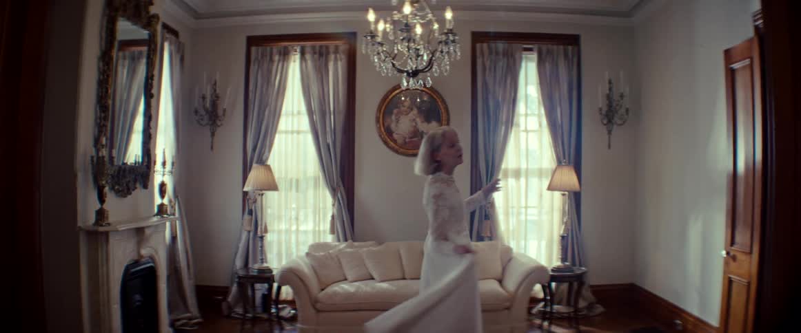 A graceful elderly woman in a vintage wedding dress dances and sings alone in an elegant living room, lost in a happy memory