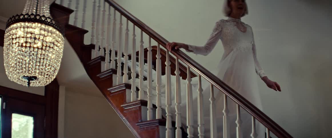 An elegant elderly bride in a white lace wedding dress gracefully descends a grand wooden staircase