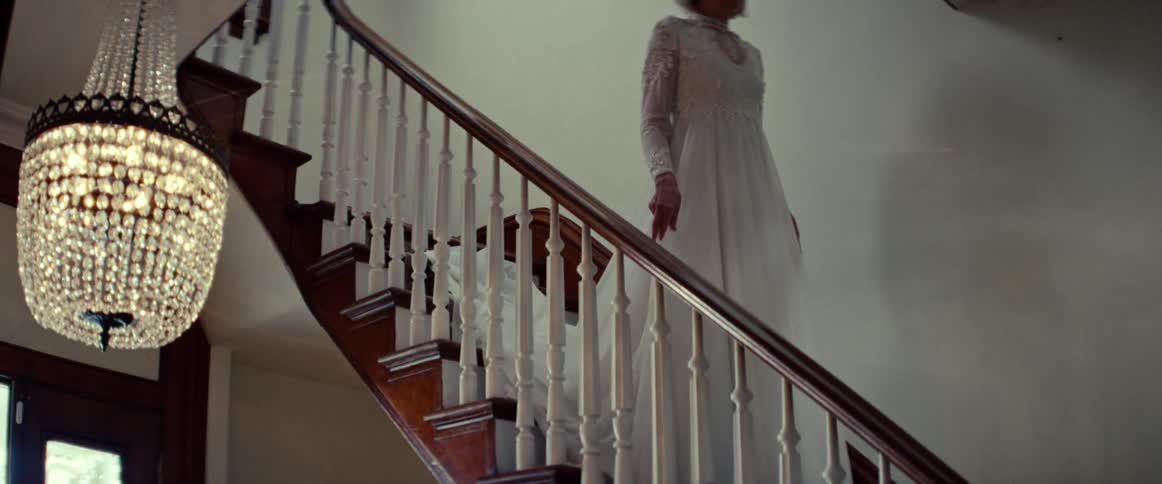 A mysterious elderly bride in a vintage white gown slowly descends a grand wooden staircase in a mansion