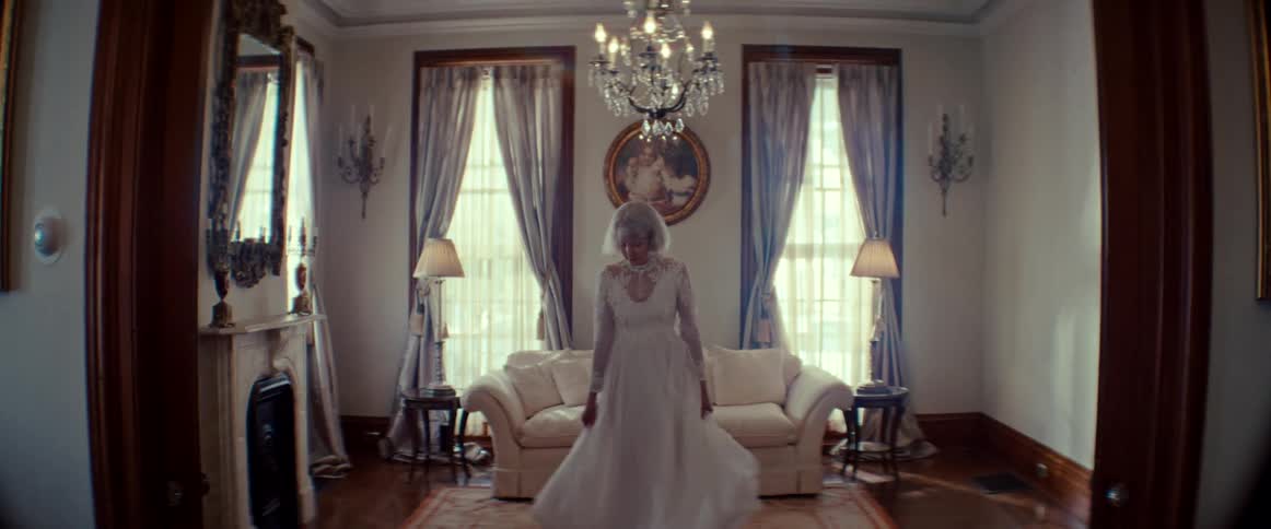 A woman in a beautiful vintage wedding dress twirls slowly in a grand, sunlit parlor