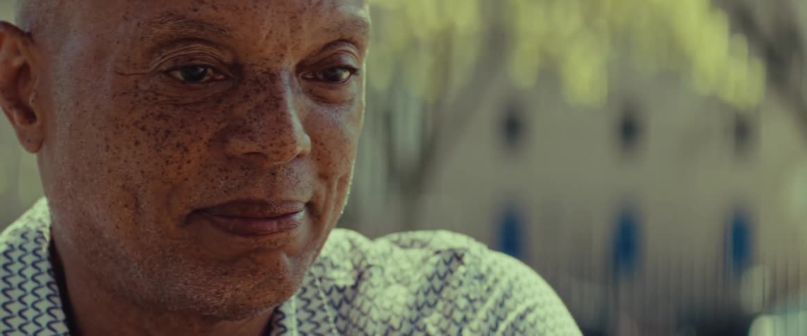 An extreme close-up of a freckled elderly Black man looking up and smiling warmly on a sunny day
