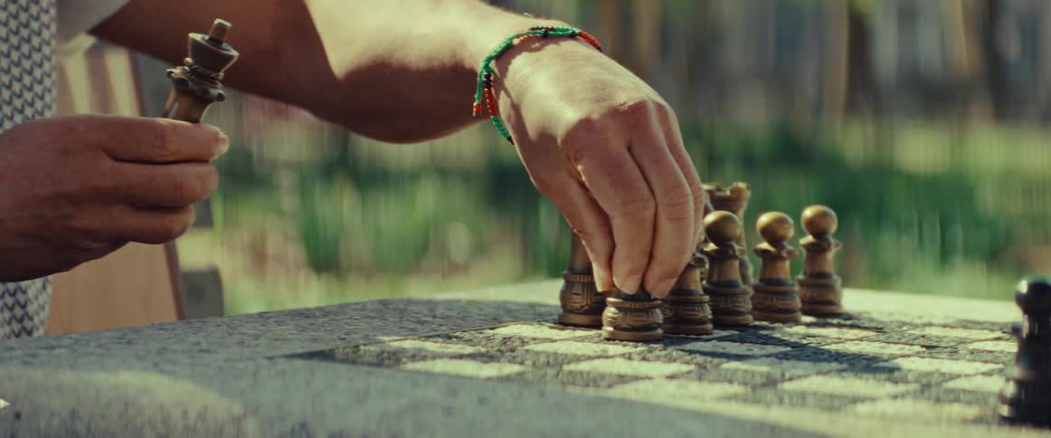 A close-up of a person's hands playing a game of chess on a stone board in a sunlit park