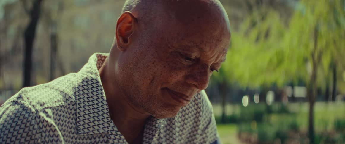 A pensive elderly Black man contemplates his next move during a game of chess in a sunny park