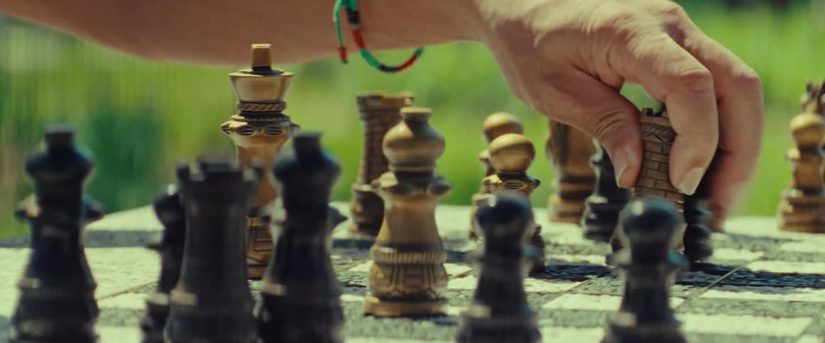A close-up shot of a hand moving a white rook on a wooden chessboard during a game in a park