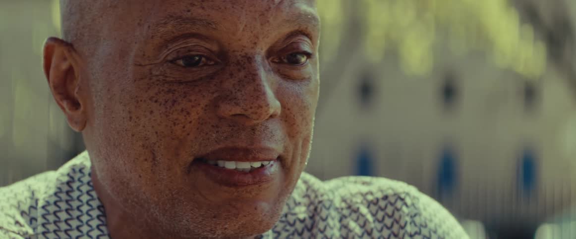 A heartwarming close-up of an older Black man with freckles smiling gently in the sunlight