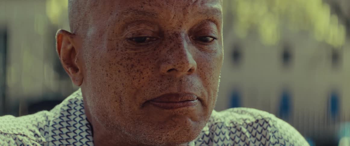 A close-up shot captures the somber and contemplative expression of an older Black man looking down