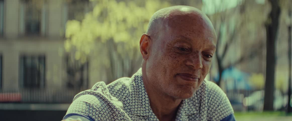 Close-up portrait of a thoughtful elderly Black man smiling warmly in a sunlit park