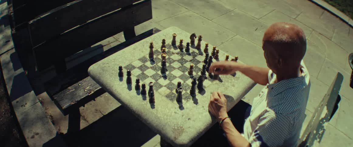 A man thoughtfully plays a game of chess by himself on a sunny day in a public square