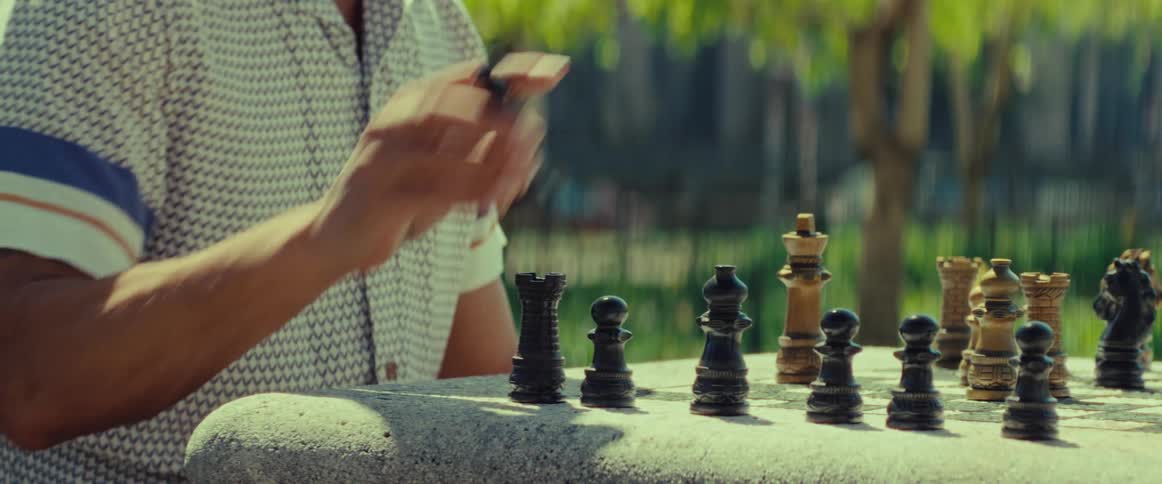 A man contemplates and makes his move during a game of chess at a stone table in a park