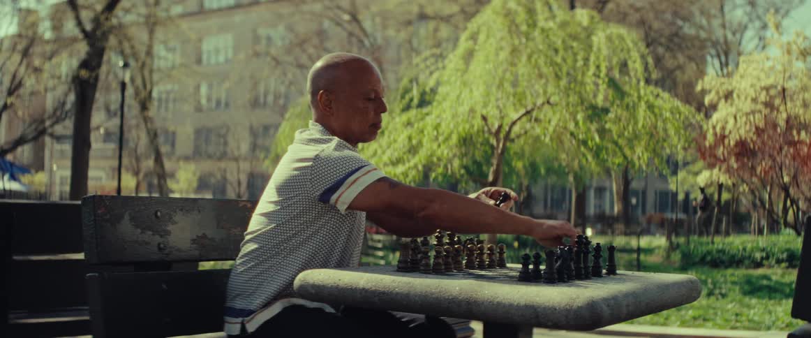A thoughtful older man plays a solitary game of chess on a park bench during a sunny afternoon