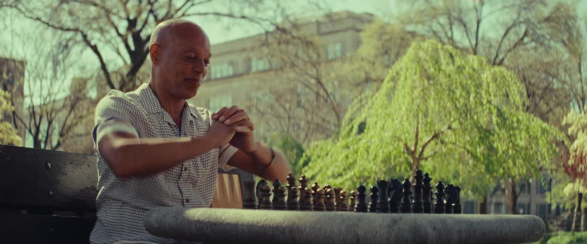 A smiling senior man stretches his hands before making a move in a solo chess game at the park
