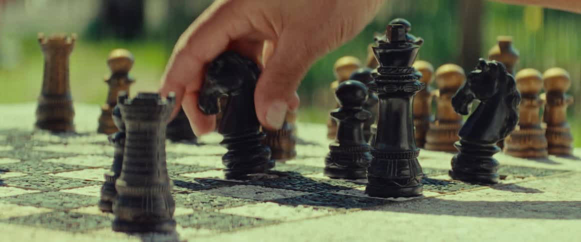 Close up of a hand making a move with the knight piece during a game of chess outdoors in the sun