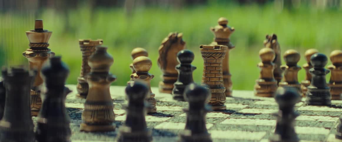 A strategic chess move is made as a hand moves a white rook on a weathered chessboard outdoors in the sunshine