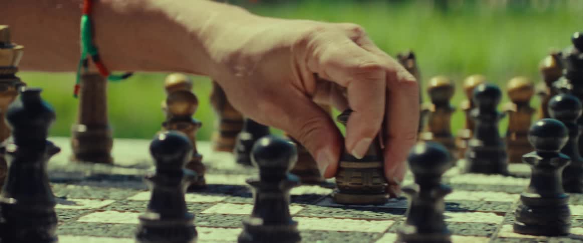 A strategic move is made with a white bishop during a chess game in a sunlit park