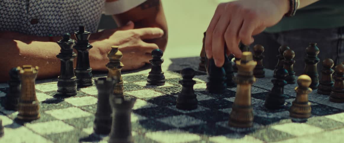 A close-up of a chess game being played outdoors in the sun, with a hand moving a knight piece