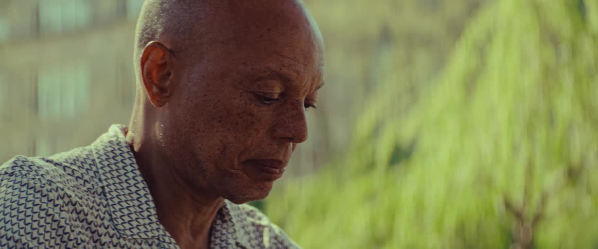 A close-up profile shot of an elderly Black man looking down with a contemplative expression on a hot day