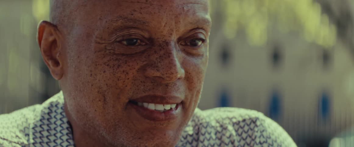 Close-up portrait of a happy, bald Black man with freckles smiling gently in the warm sunlight
