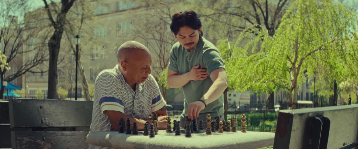 Two men of different generations bond over a friendly game of chess in a sunny city park