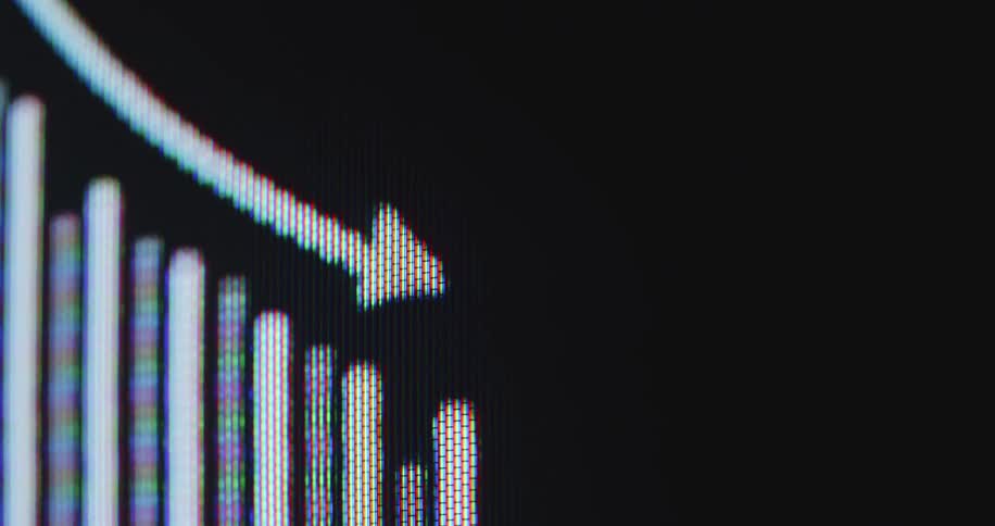 A macro view of a digital screen displays a falling stock market chart with a downward trend arrow