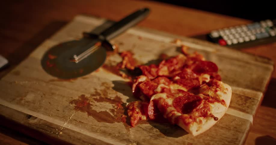 Close up static shot of messy leftover pepperoni pizza on a wooden cutting board with a pizza cutter