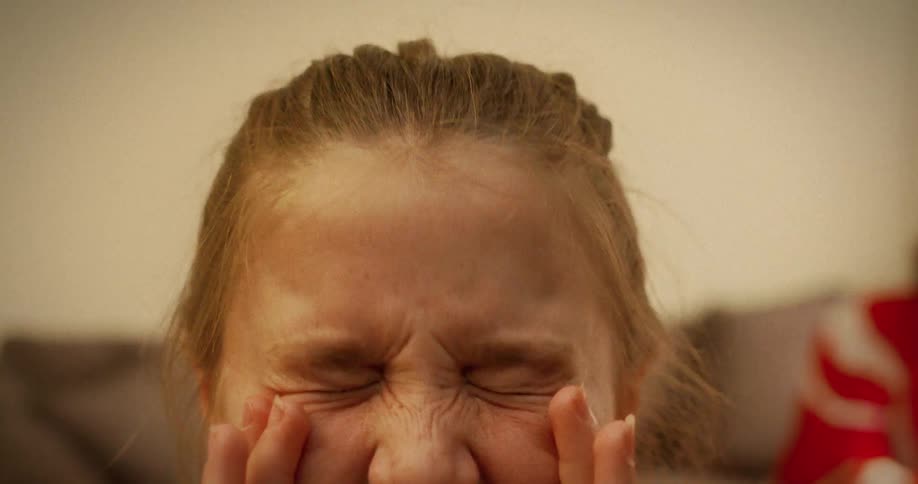 A tired young girl with strained, red eyes rubs them and squeezes them shut as if in pain