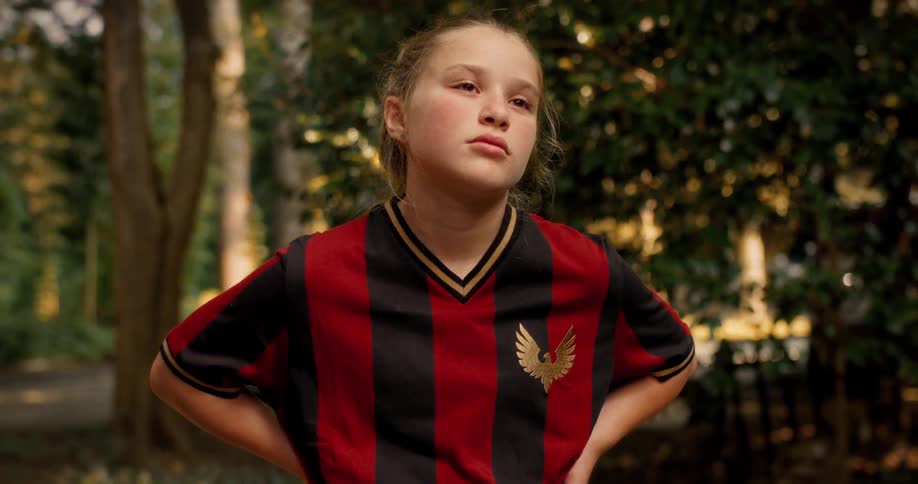 A determined young female soccer player stands outside, takes a deep breath, and focuses before a game