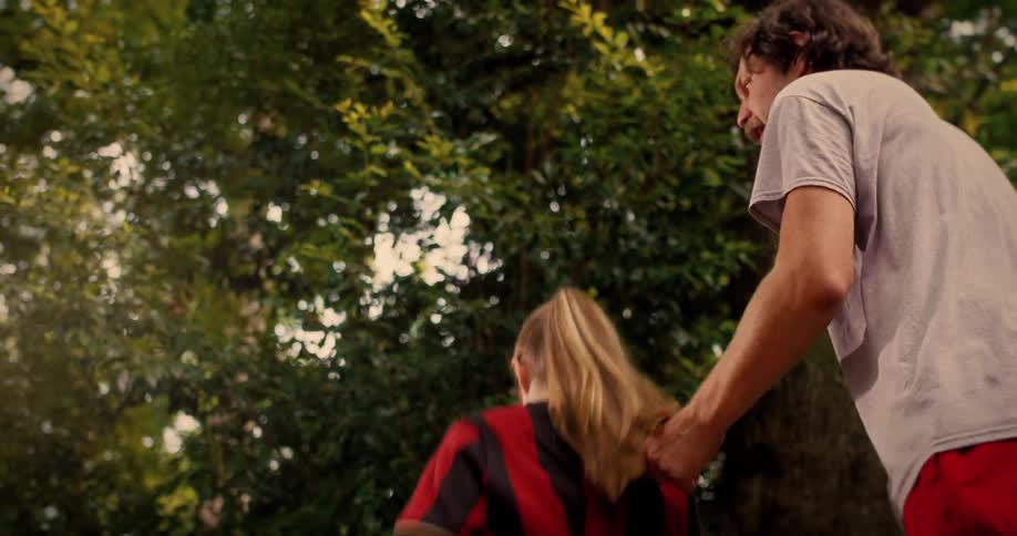 A young girl in a soccer jersey gets a high-five from her father before they playfully run off together in a park