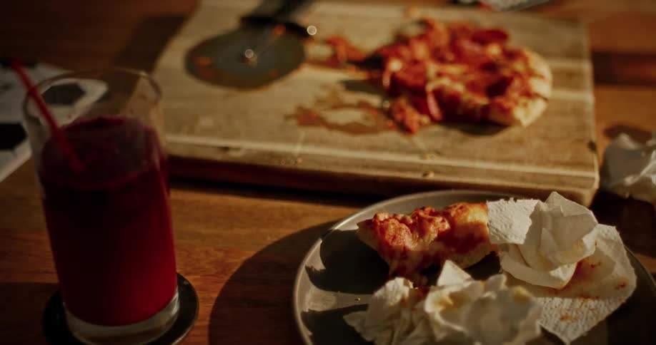 The messy remains of a pepperoni pizza and a red smoothie sit on a wooden table after a meal