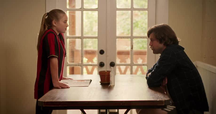 A cinemagraph of a father and his daughter in a soccer uniform having a serious talk at the kitchen table