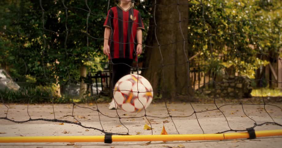 Determined young girl kicks a soccer ball into the goal, captured in a dynamic slow-motion shot from behind the net