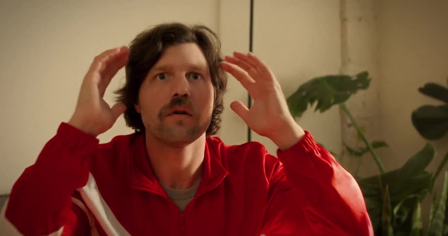 A sports fan with a mustache and red tracksuit anxiously watches a game, reacting with shock and despair