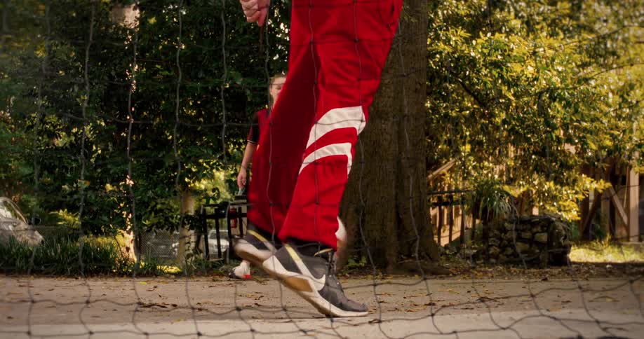 A person in a red tracksuit skillfully juggles a soccer ball in slow motion as a young girl in a jersey watches