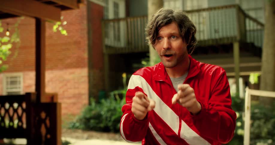 A quirky man with a mustache in a red retro tracksuit challenges the viewer before starting a game of badminton