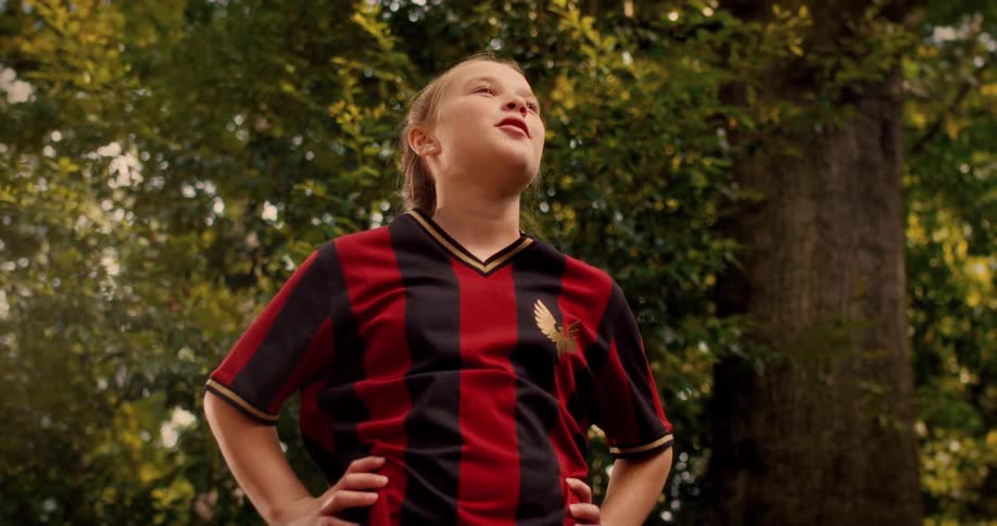 A fierce young girl in a soccer uniform unleashes a powerful kick and a triumphant shout in slow motion