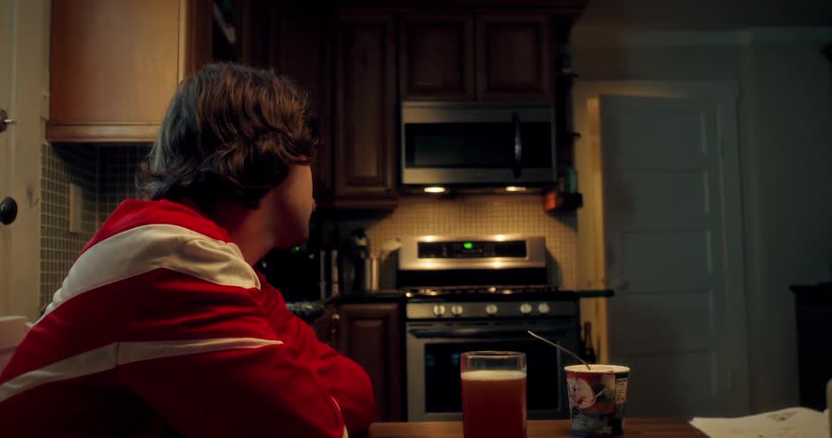 A supportive father comforts his sad daughter in her soccer jersey at the kitchen table at night